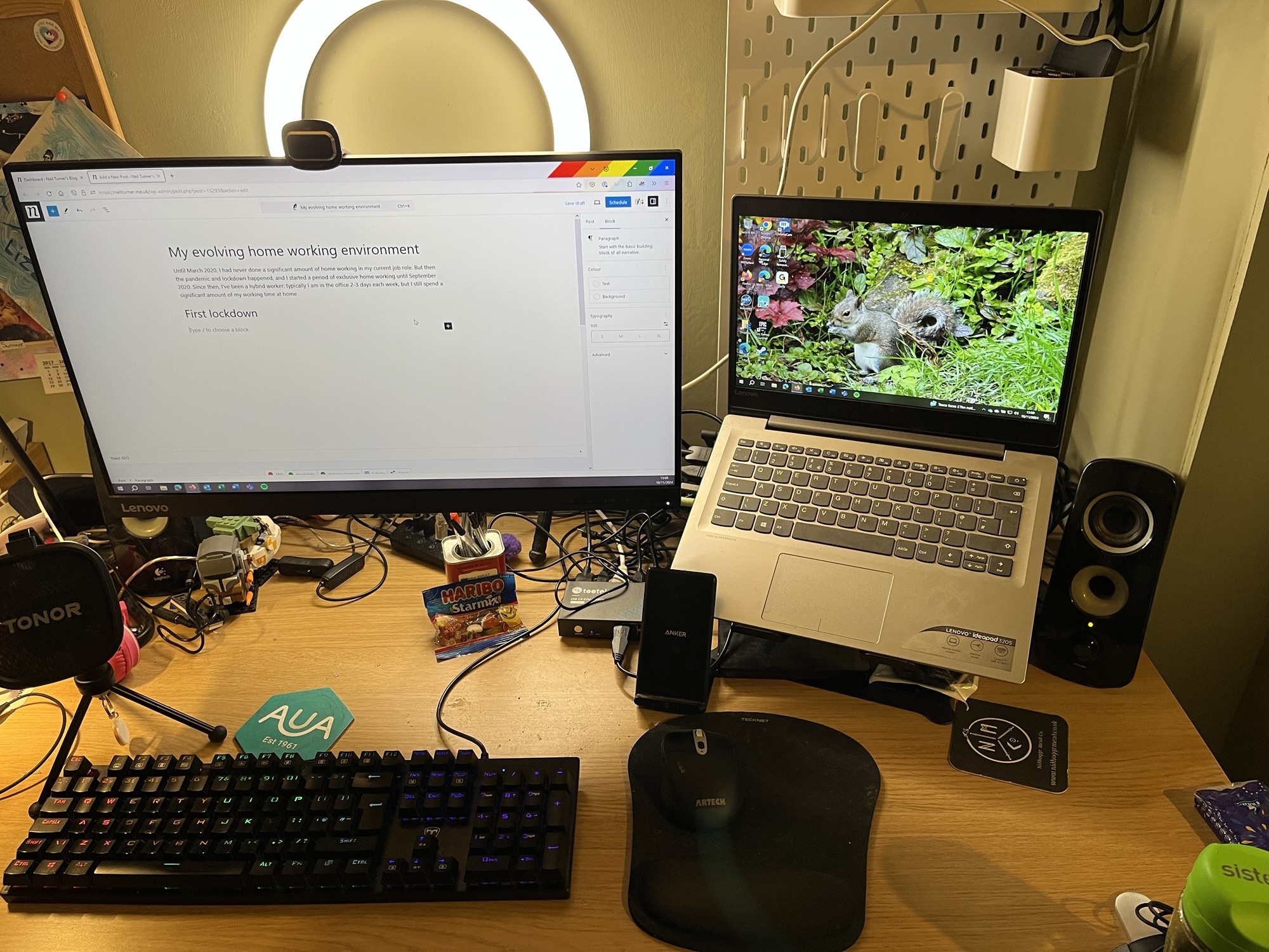 A photo of my home working environment. There is a large LED screen on the left, and a laptop on the right. In the foreground, there is a keyboard and mouse. and a ring light behind.