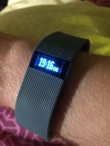A photo of a Fitbit Charge. It's on my wrist and shows the time as 19:16
