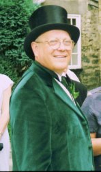 A photo of John Bramham at his daughter's wedding. He's wearing a green suit and a top hat