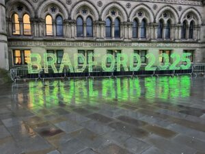 A photo of some large illuminated letters spelling out 'Bradford 2025' in green, outside Bradford City Hall