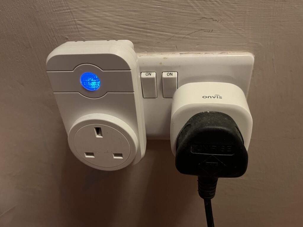 A Tuya smart plug (on the left) next to a Onvis smart plug (on the right) both plugged in to a wall socket